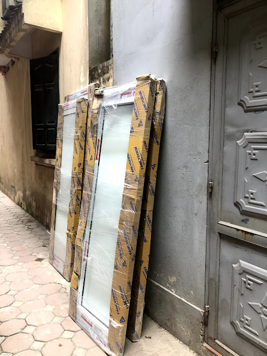 Cửa kính khung nhôm mới bọc carton dựng sát tường trong ngõ nhỏ